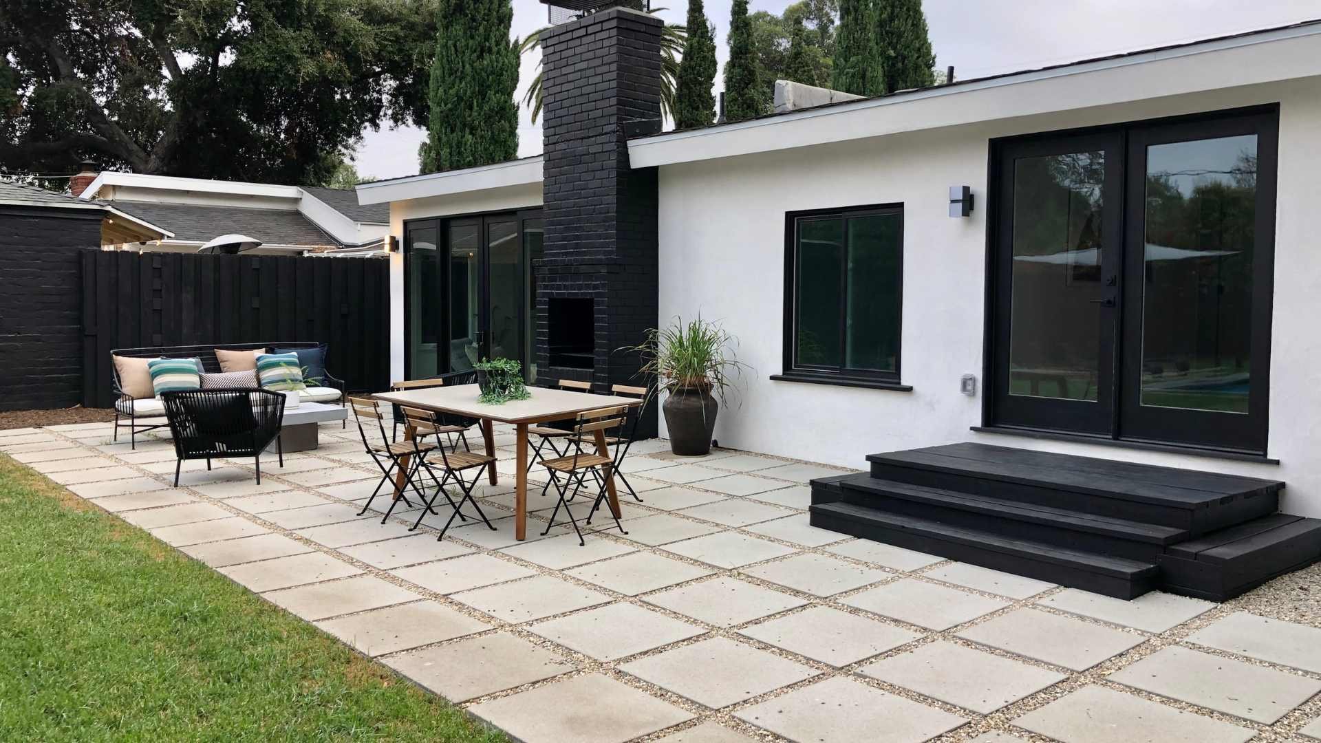 Modern patio area with outdoor dining and seating leading to a rectangular pool in a minimalist backyard.