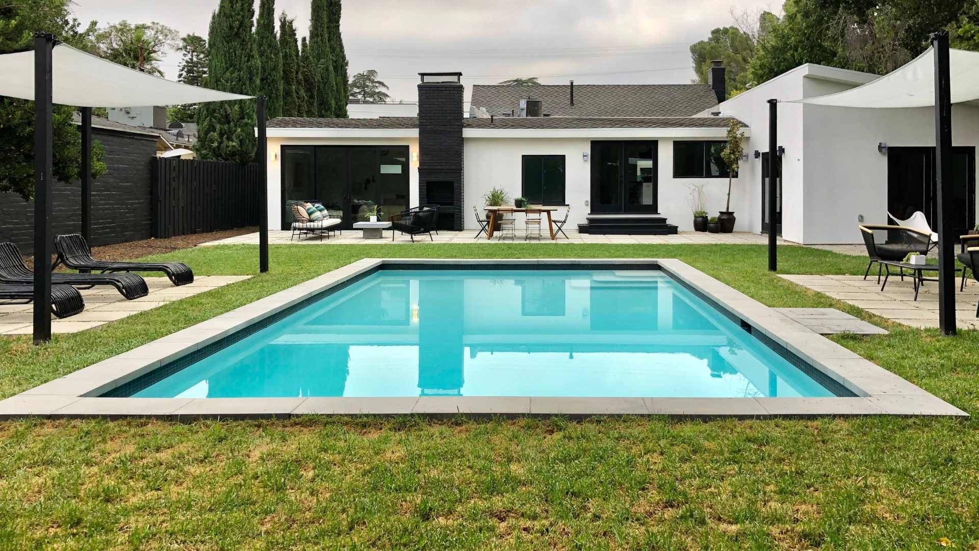 A modern backyard featuring a rectangular pool with precast coping, surrounded by a green lawn and a contemporary house in the background.