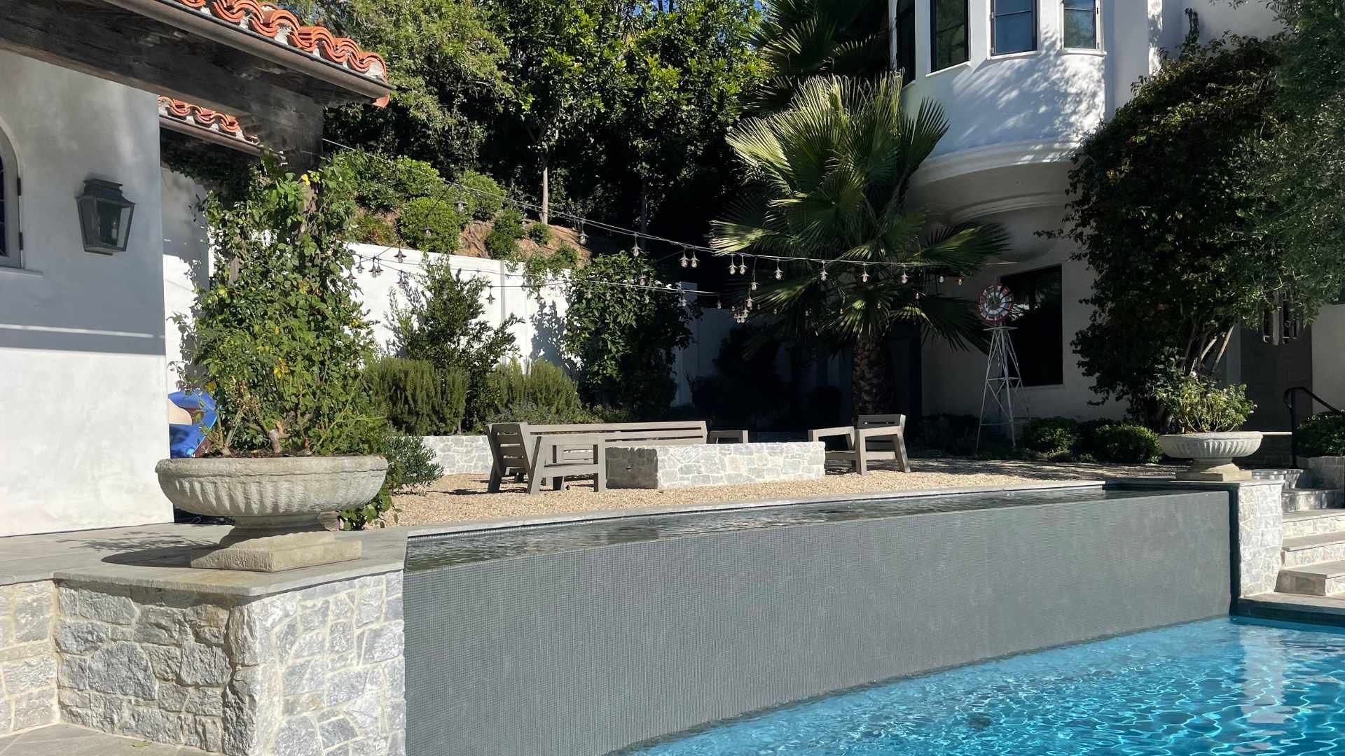 Poolside water features fountains and stone detailing adjacent to a charming white cottage with a tiled roof.