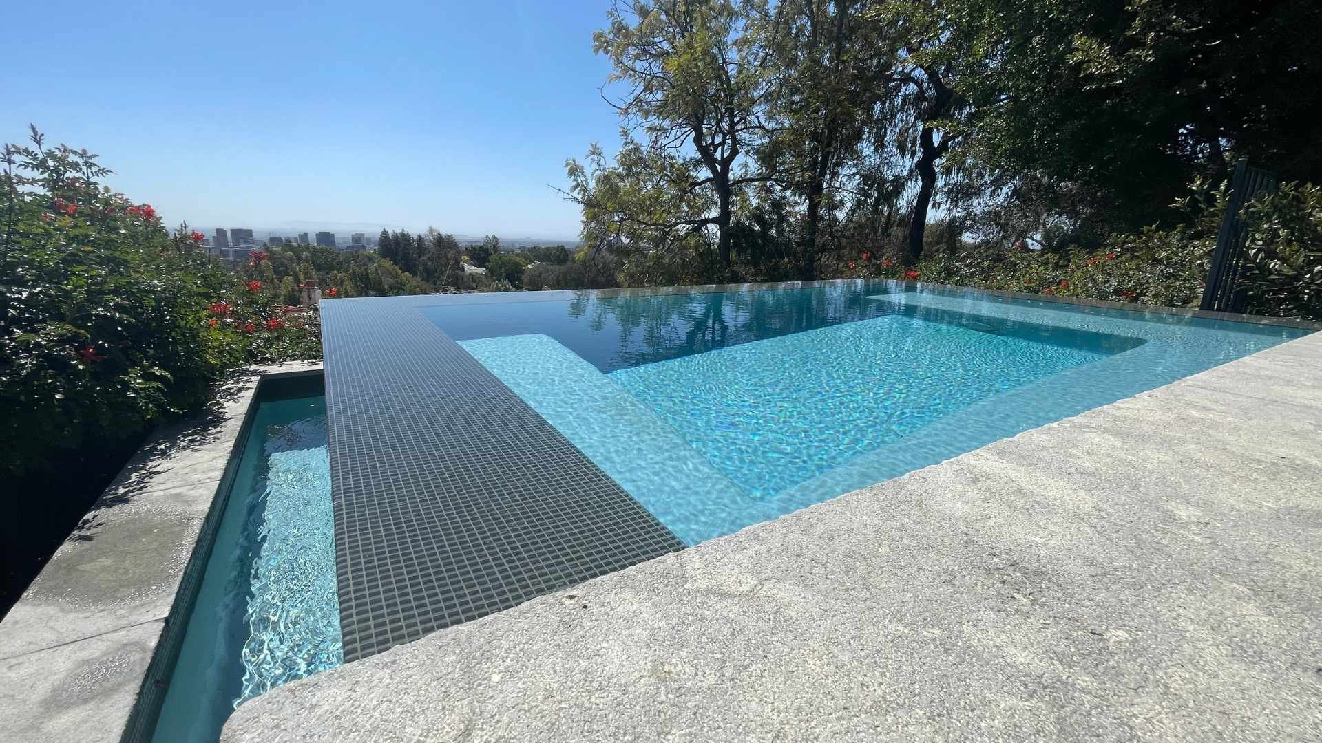 Infinity spa with a sleek design, surrounded by vibrant greenery, offering a view of the hillside and city below.