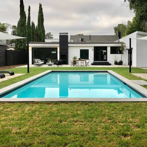 A modern backyard featuring a rectangular pool with precast coping, surrounded by a green lawn and a contemporary house in the background.