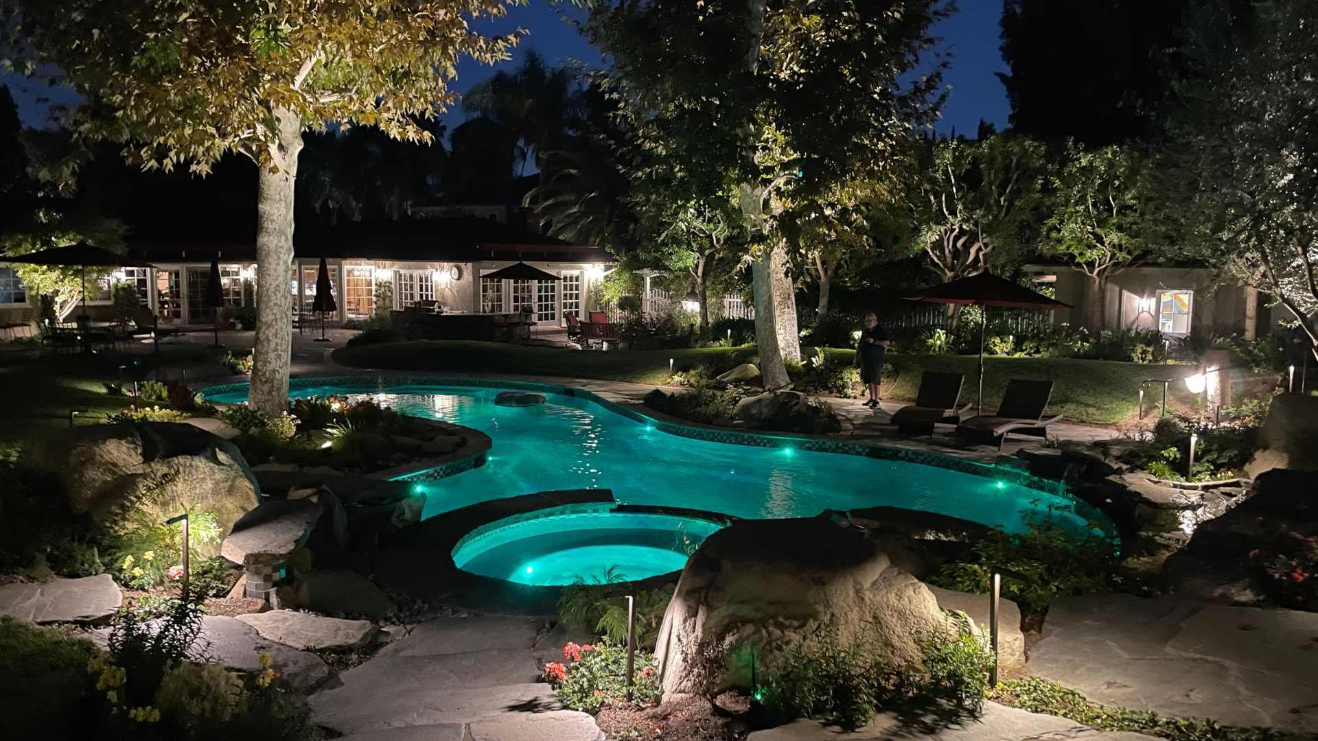 Evening ambiance around a backyard pool illuminated by soft landscape lighting, creating a serene atmosphere.