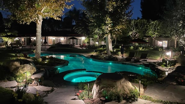Evening ambiance around a backyard pool illuminated by soft landscape lighting, creating a serene atmosphere.