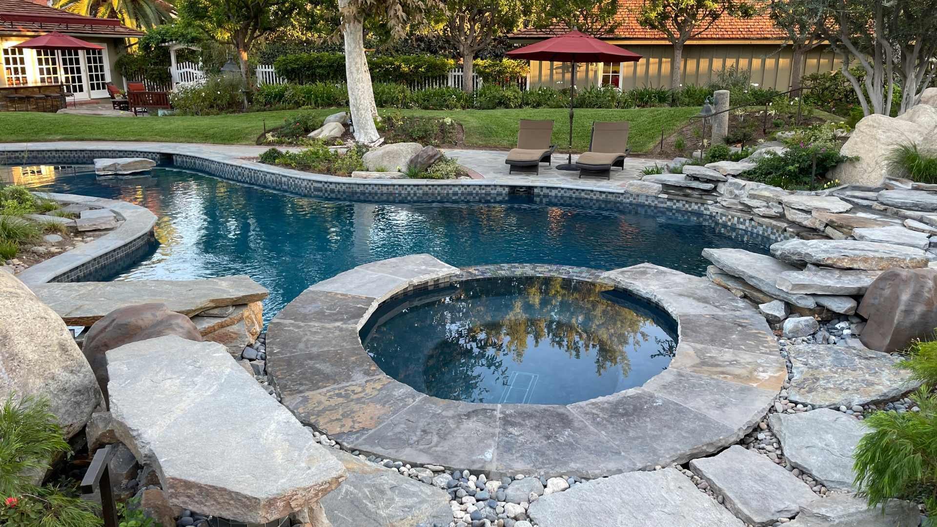Close-up of a raised spa integrated into a natural stone coping pool with surrounding rock features and glass tile accents.