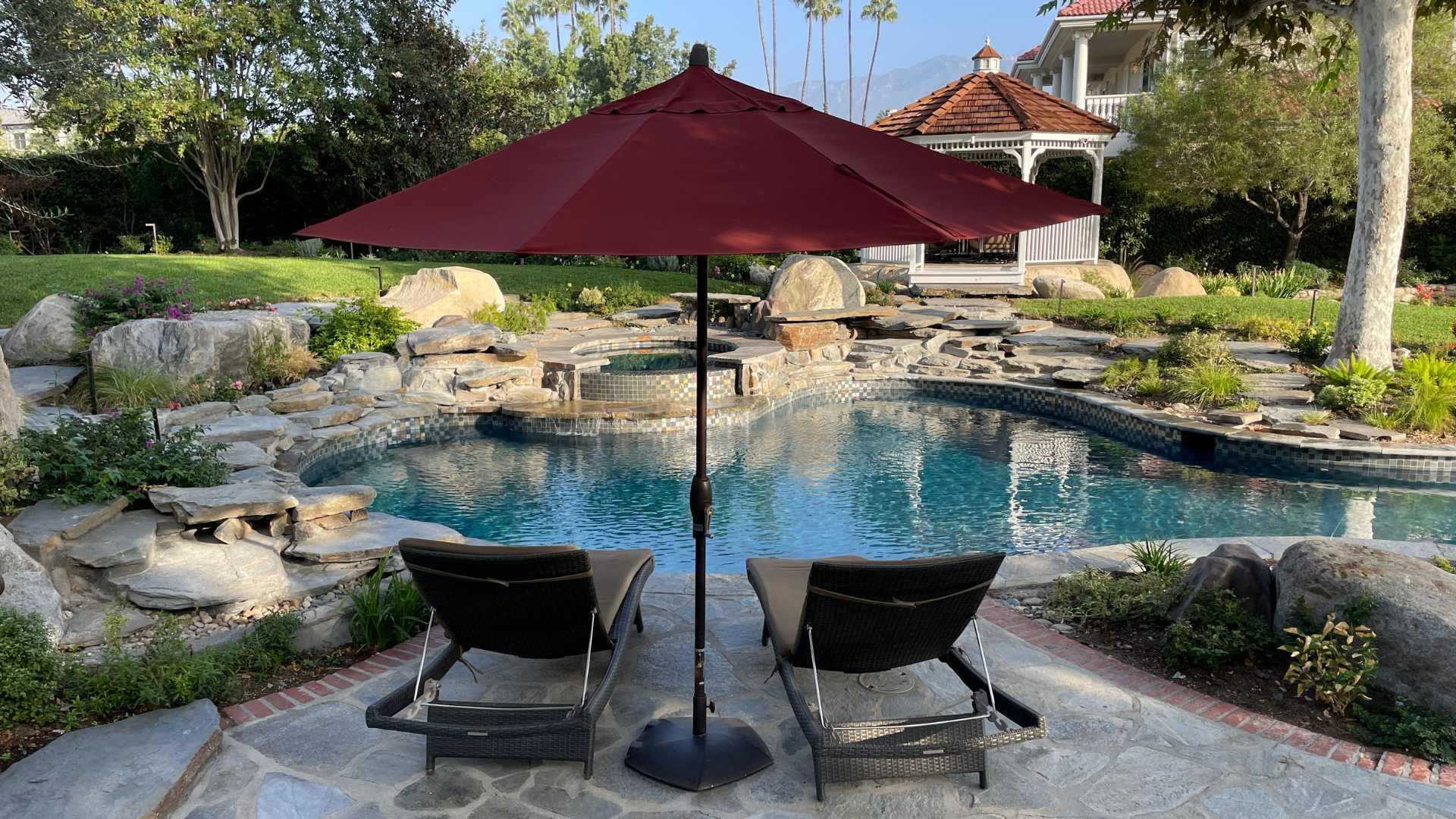 The backyard oasis features a natural stone pool, a raised spa, and a lush landscape with mature trees and colorful flowers.