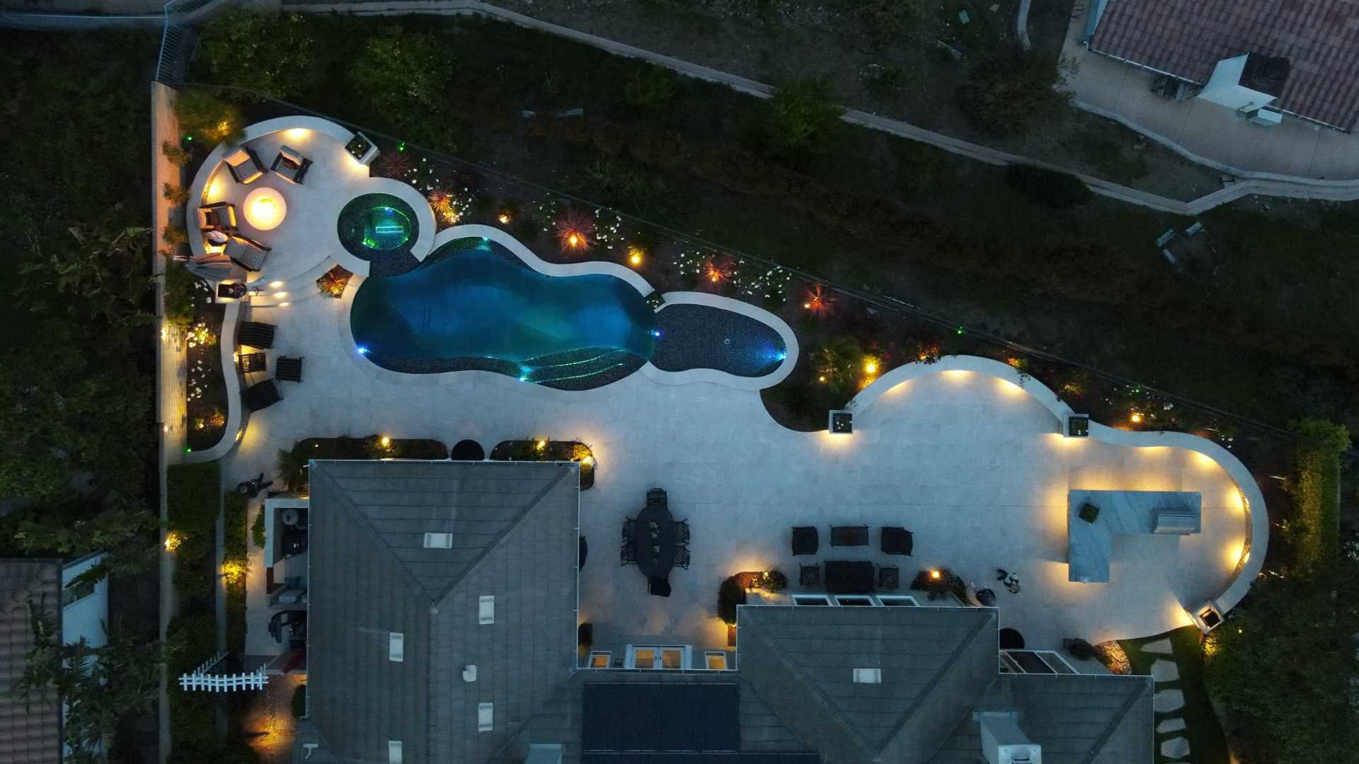 Nighttime aerial view of the entire backyard showcasing the illuminated pool, spa, and surrounding landscaping.