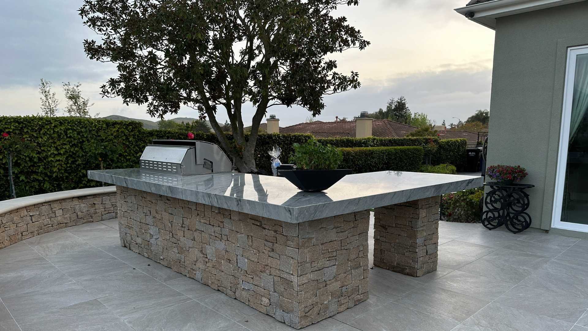 Outdoor kitchen and BBQ area with a stone base and granite countertop, set on a spacious patio.