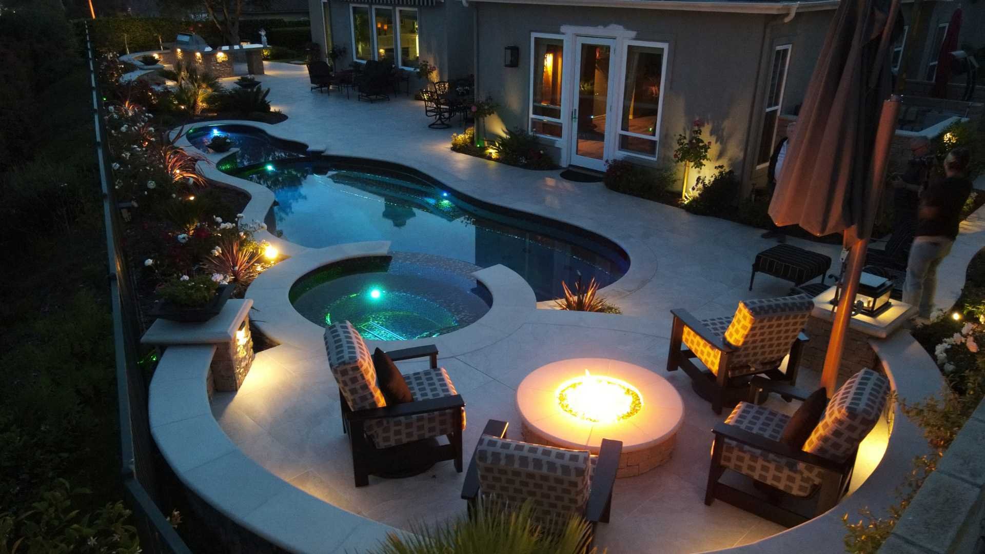The fire pit with glowing embers provides warmth to a cozy seating area next to the pool and spa.
