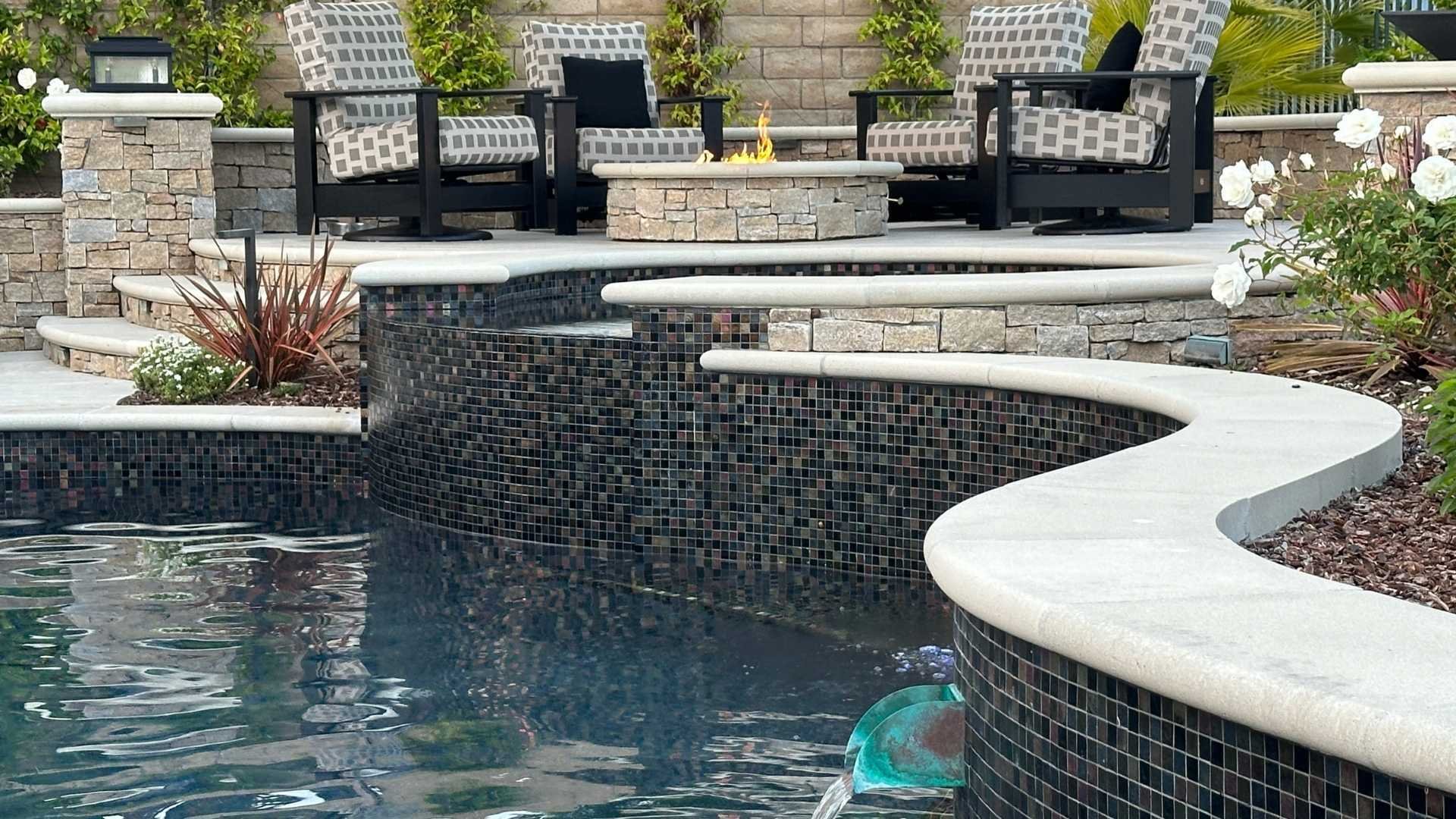 Detail of the fire pit and seating area adjacent to the pool, with a focus on the mosaic glass tiles and water feature.