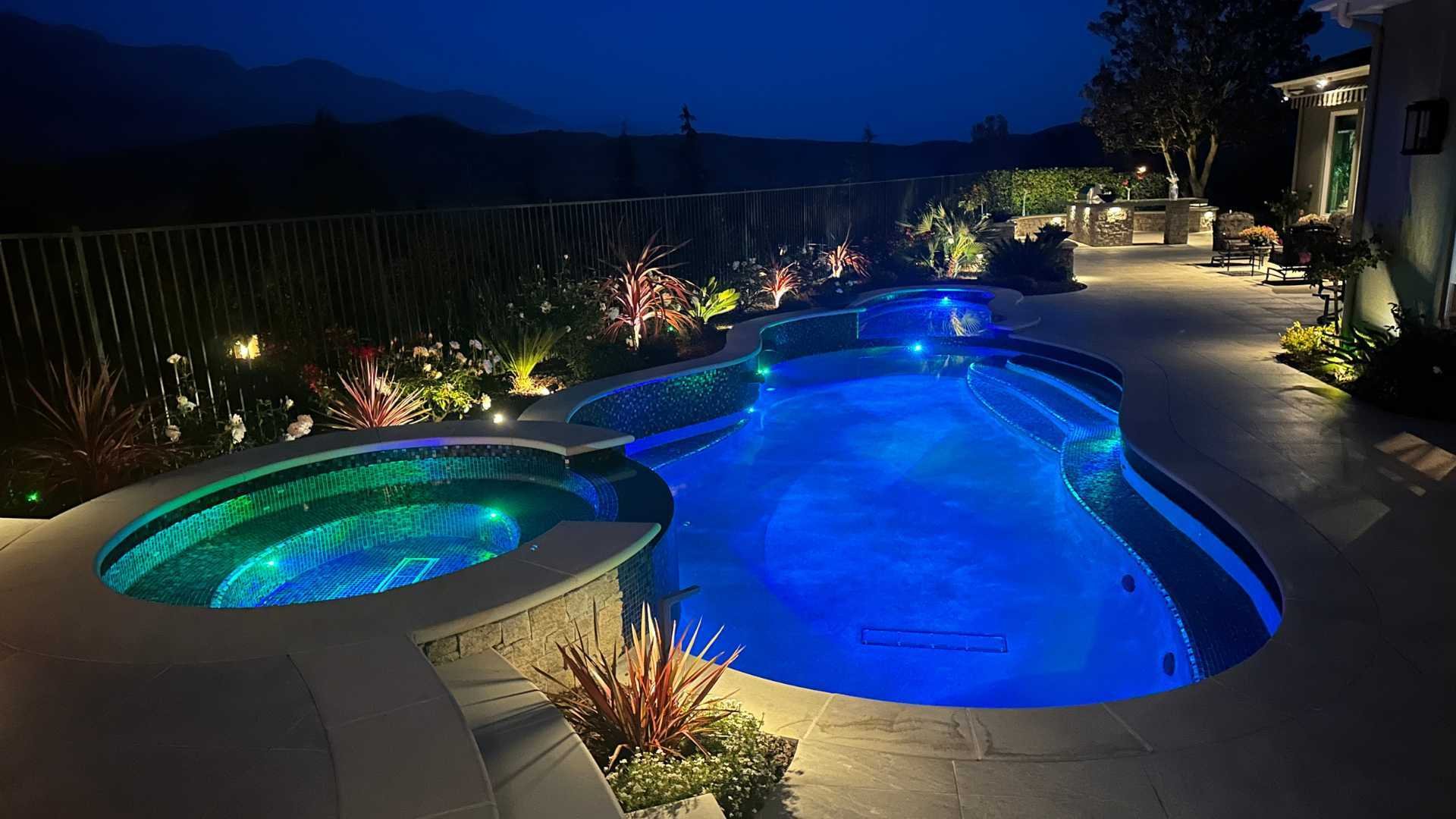 Nighttime view of the pool and spa illuminated with colorful LED lights, creating a serene ambiance.