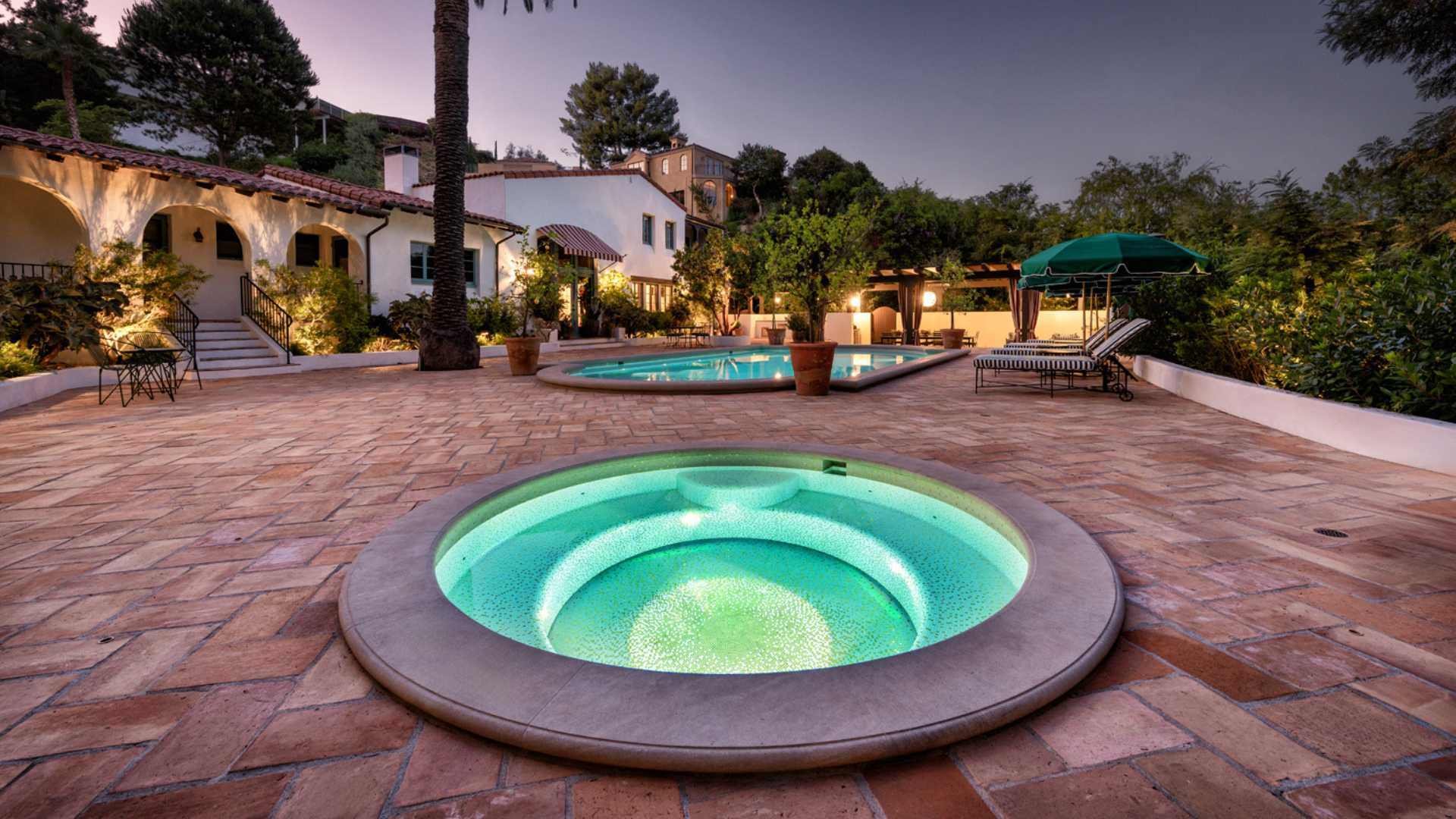 A Hollywood property with a spa and fully tiled pool, illuminated by LED lights set against Mediterranean-style landscaping