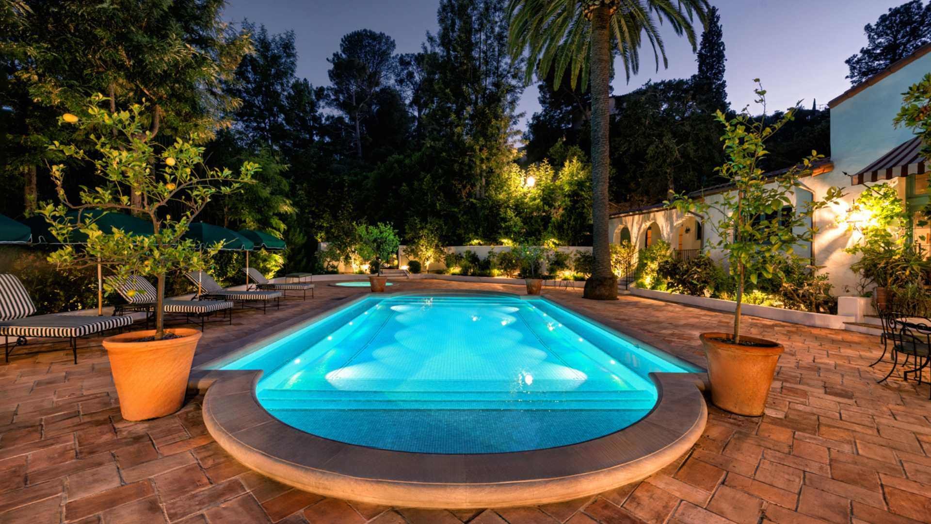 A fully tiled Mediterranean-style pool illuminated by 10 Hayward LED lights, surrounded by lush greenery and a warm ambiance, is located in Hollywood.