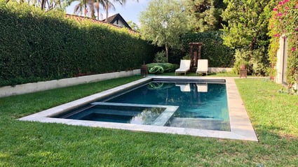 A private backyard pool surrounded by greenery, with comfortable lounge chairs and a patio covered in vibrant bougainvillea.