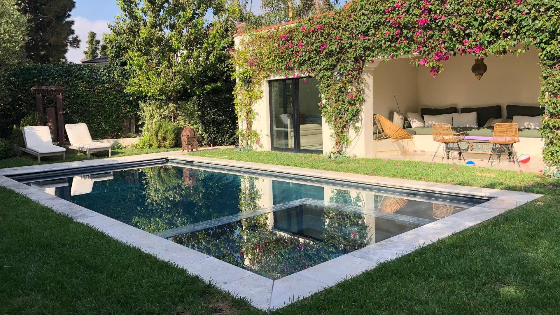 Backyard pool area with lush greenery featuring a patio draped in bougainvillea and a shaded seating nook.