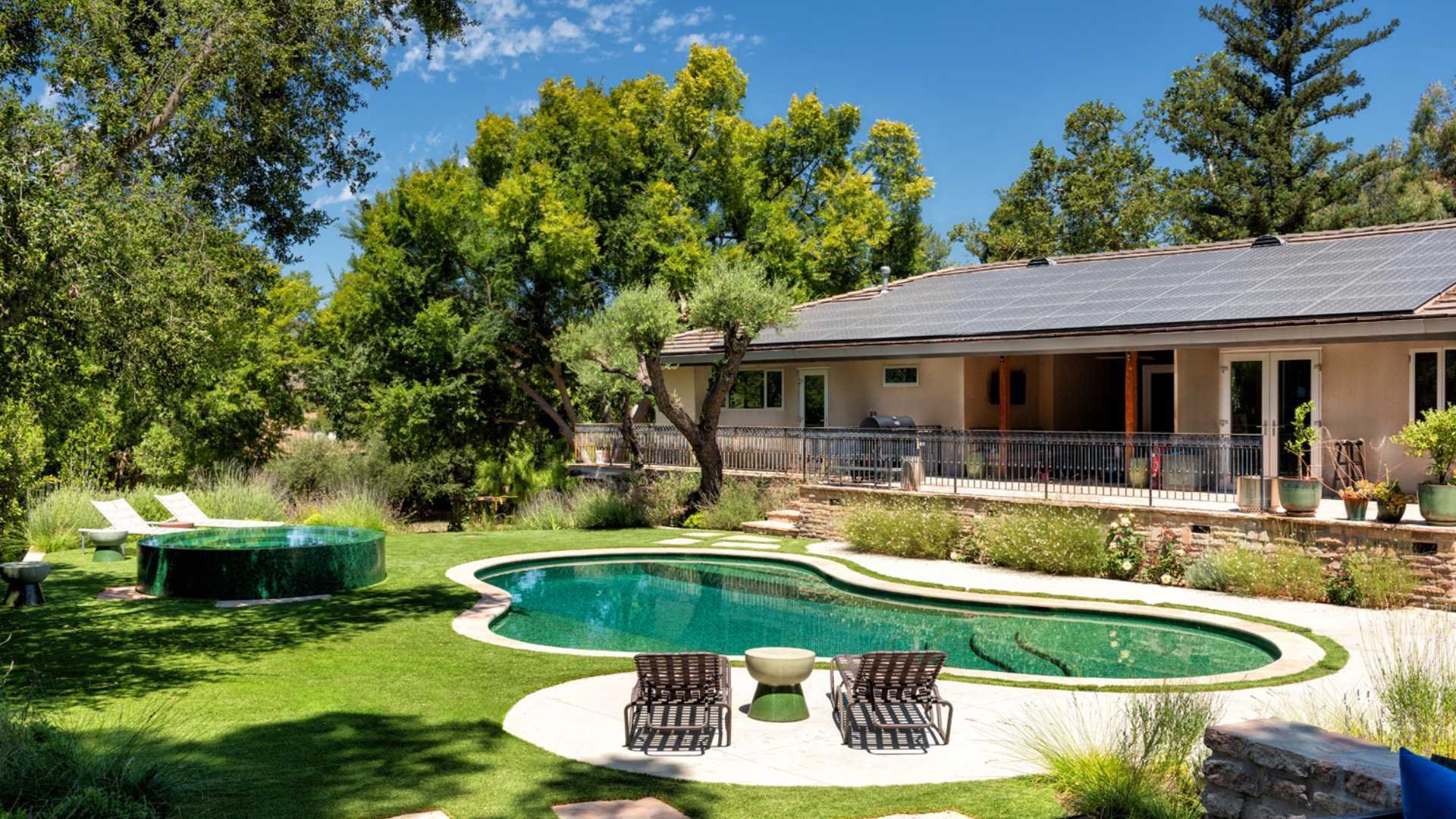 A backyard view of a Calabasas property showcasing a fully tiled pool and raised round spa, with outdoor seating areas.