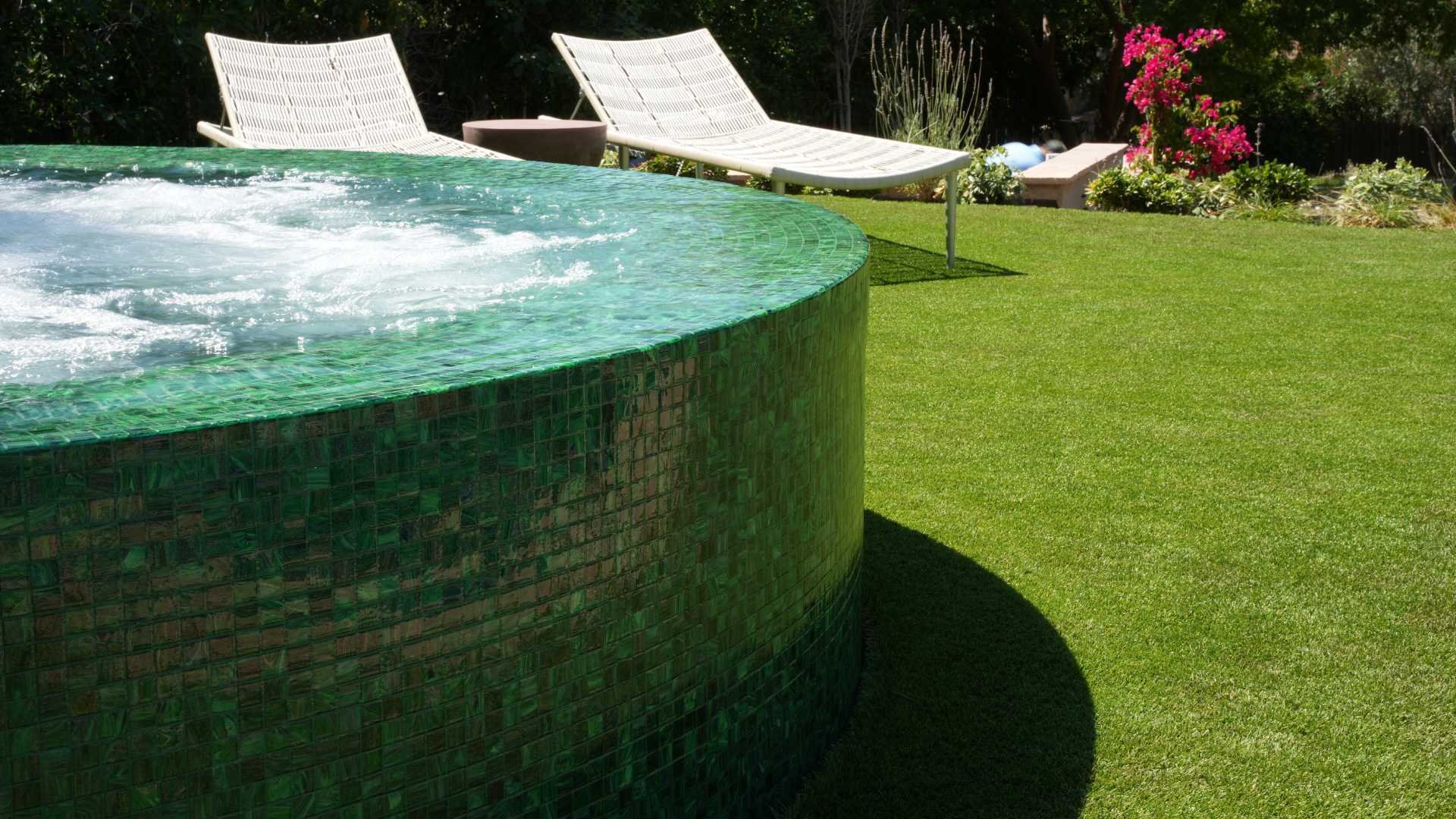 Side view of a round, fully tiled overflow perimeter spa, surrounded by a manicured lawn in a Calabasas property.