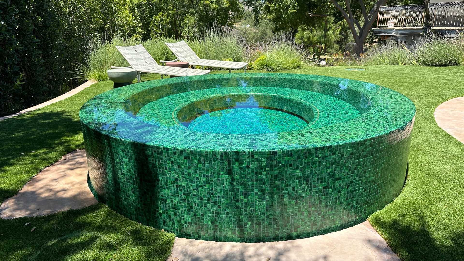 A fully tiled round overflow perimeter spa in a verdant Calabasas property, bathed in daylight.