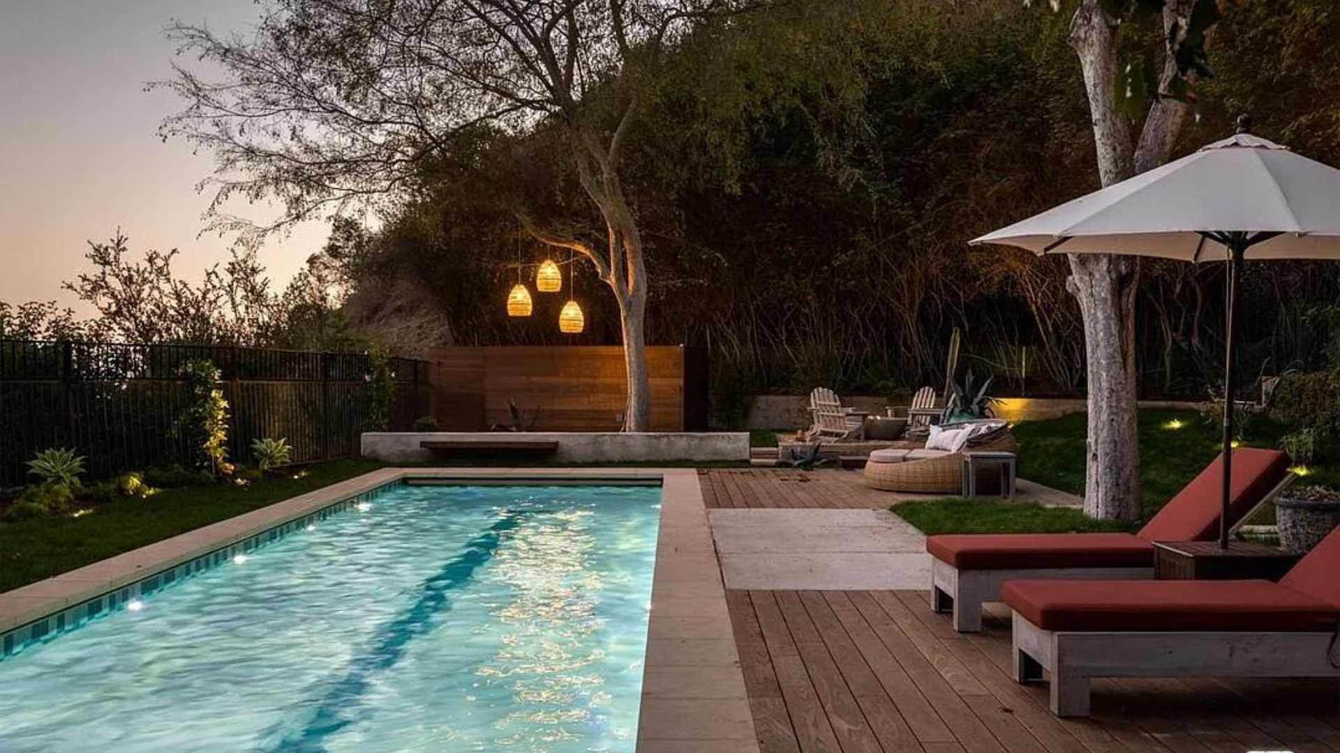 Long, narrow lap pool with a central lane marker, bordered by trees and lounge chairs, illuminated