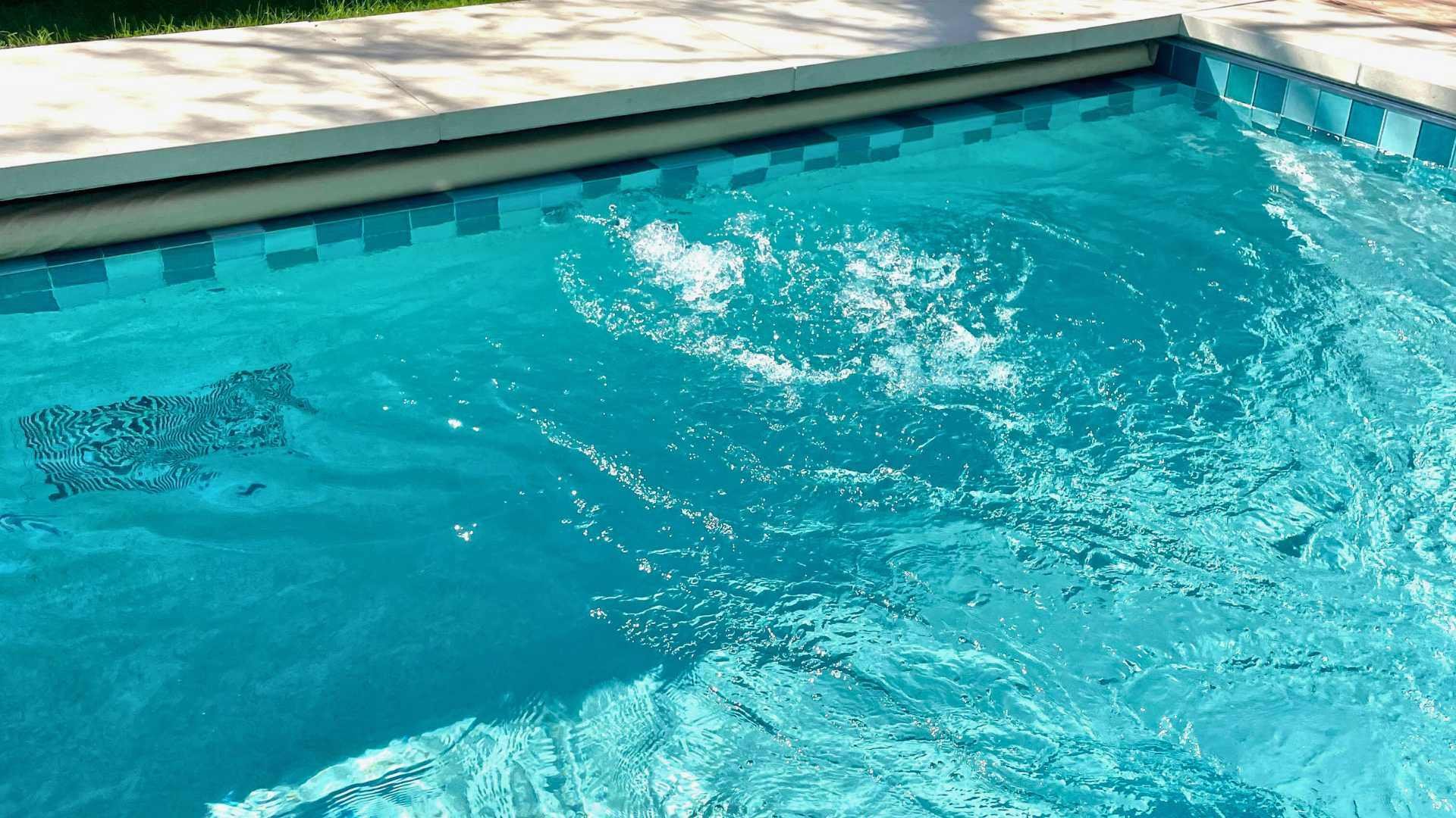 Close-up view of river flow current in a lap pool, with a grassy area and outdoor seating in the background.