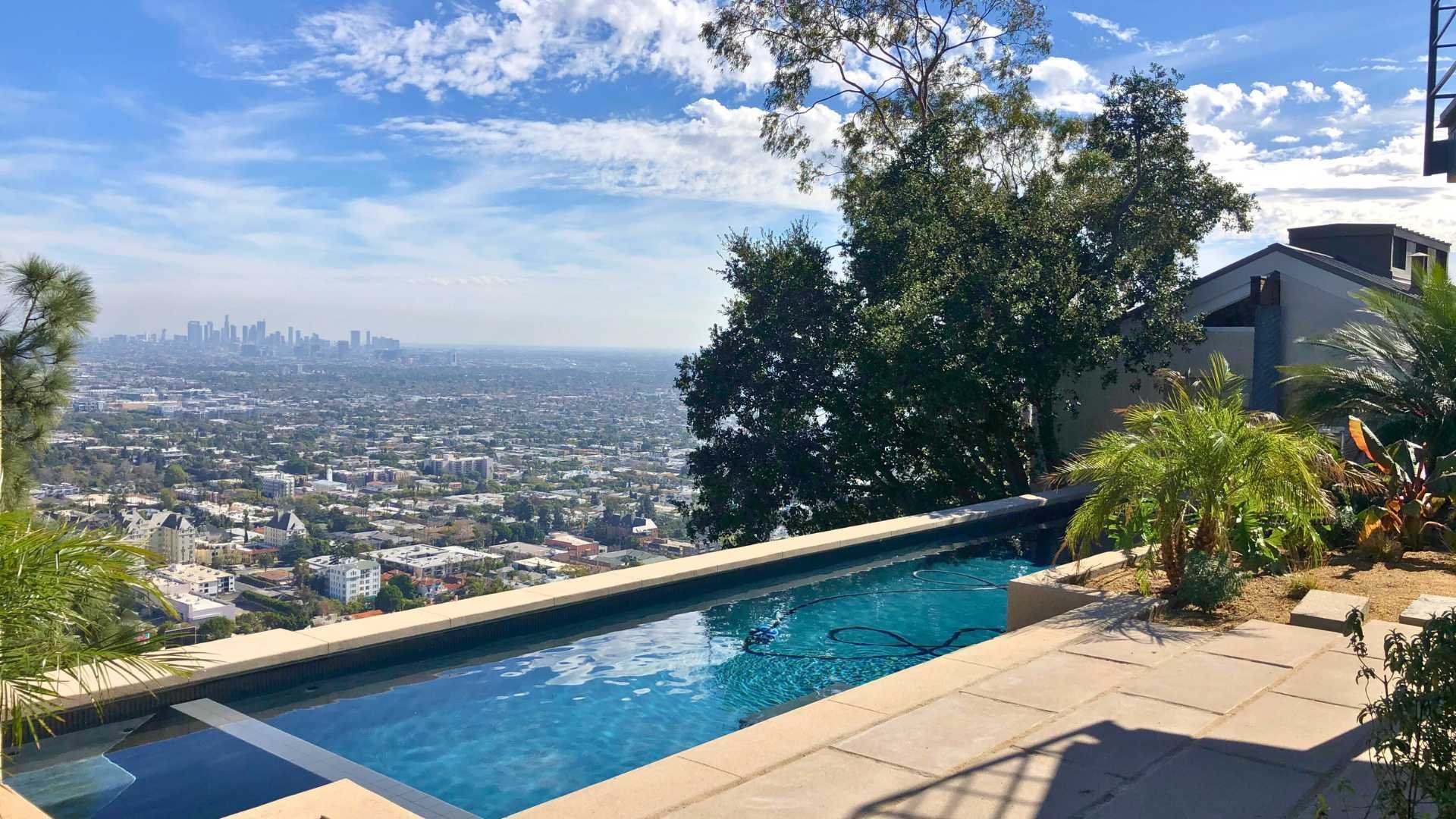 The hillside lap pool offers panoramic views of the Los Angeles skyline under a clear blue sky.