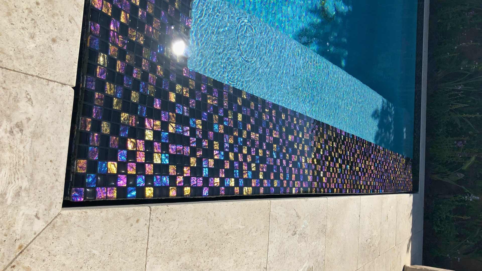 Close-up of lightstream glass tiles lining the perimeter of the overflow spa, shimmering under sunlight.