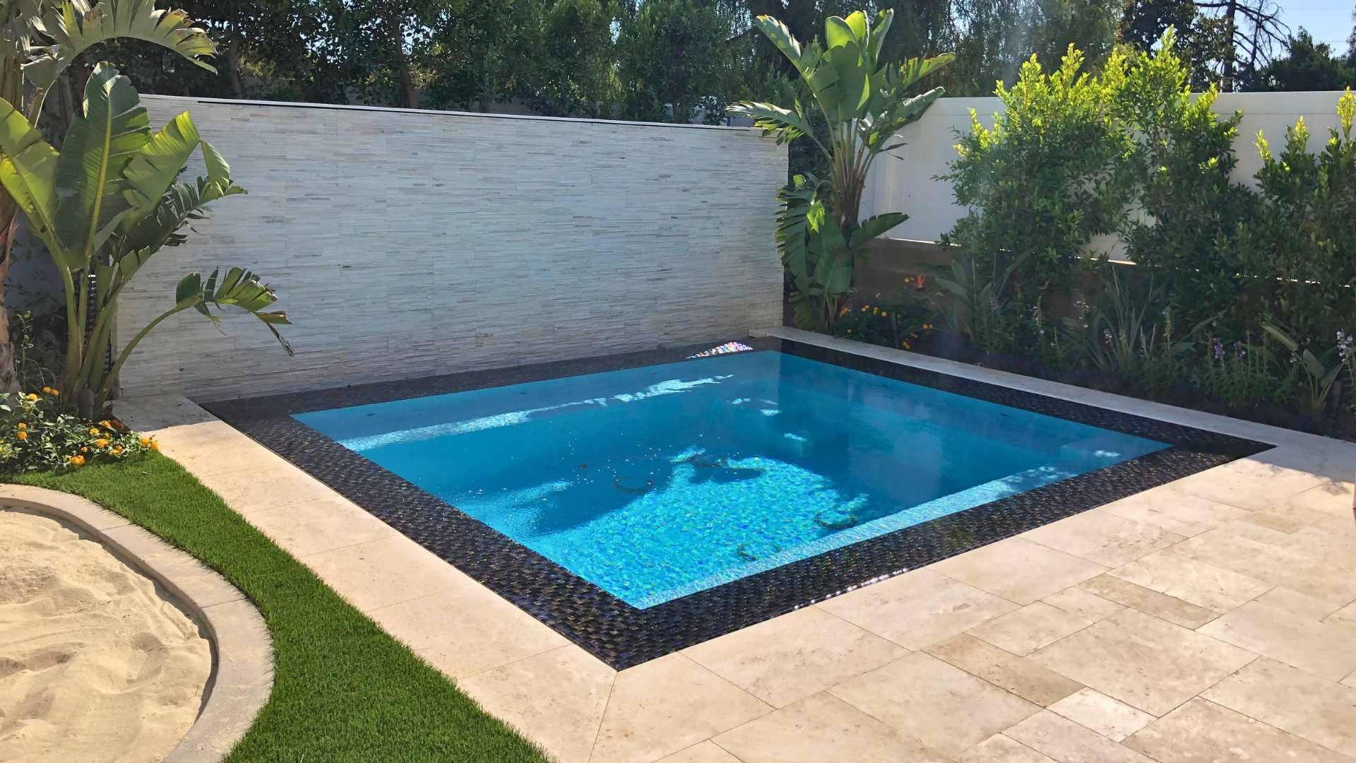 Wide shot of an overflow perimeter spa with a water wall and tropical plants in a modern backyard.