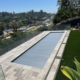 Automatic pool cover in place over a modern pool with a glass railing and Greek marble deck in Silver Lake 