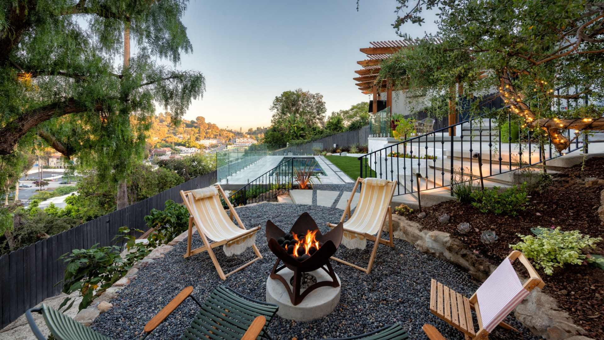 A cozy fire pit area with outdoor seating overlooks a luxurious hillside pool and pergola in a Silver Lake backyard.