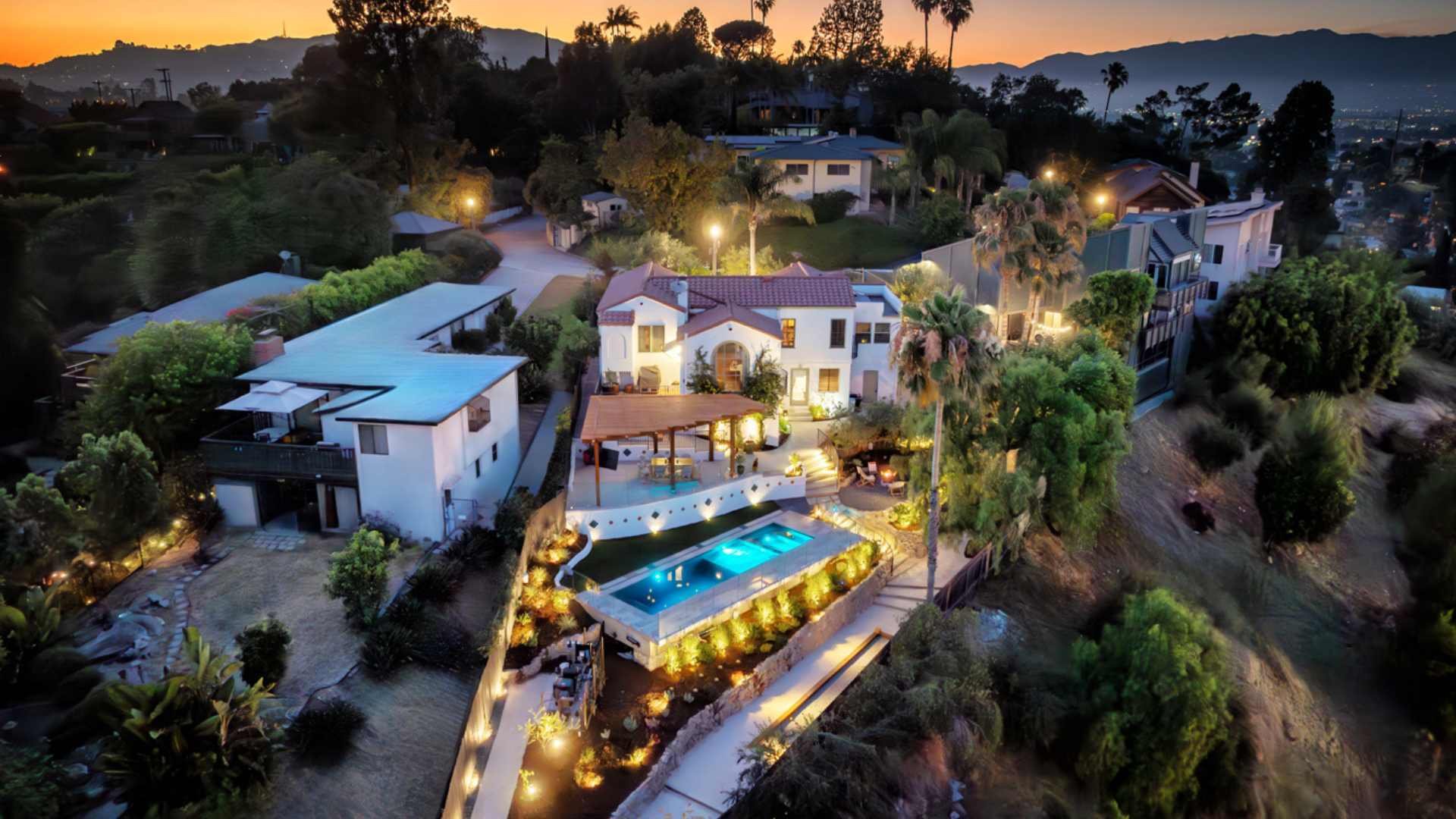 Dusk shot of luxurious hillside property in Silver Lake, showcasing an illuminated pool with glass railing and a panoramic view.
