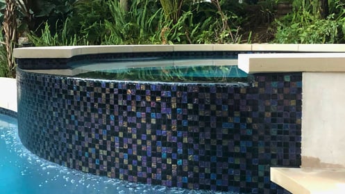 Detail of the raised spa with shimmering glass tiles and water cascading into the pool below.