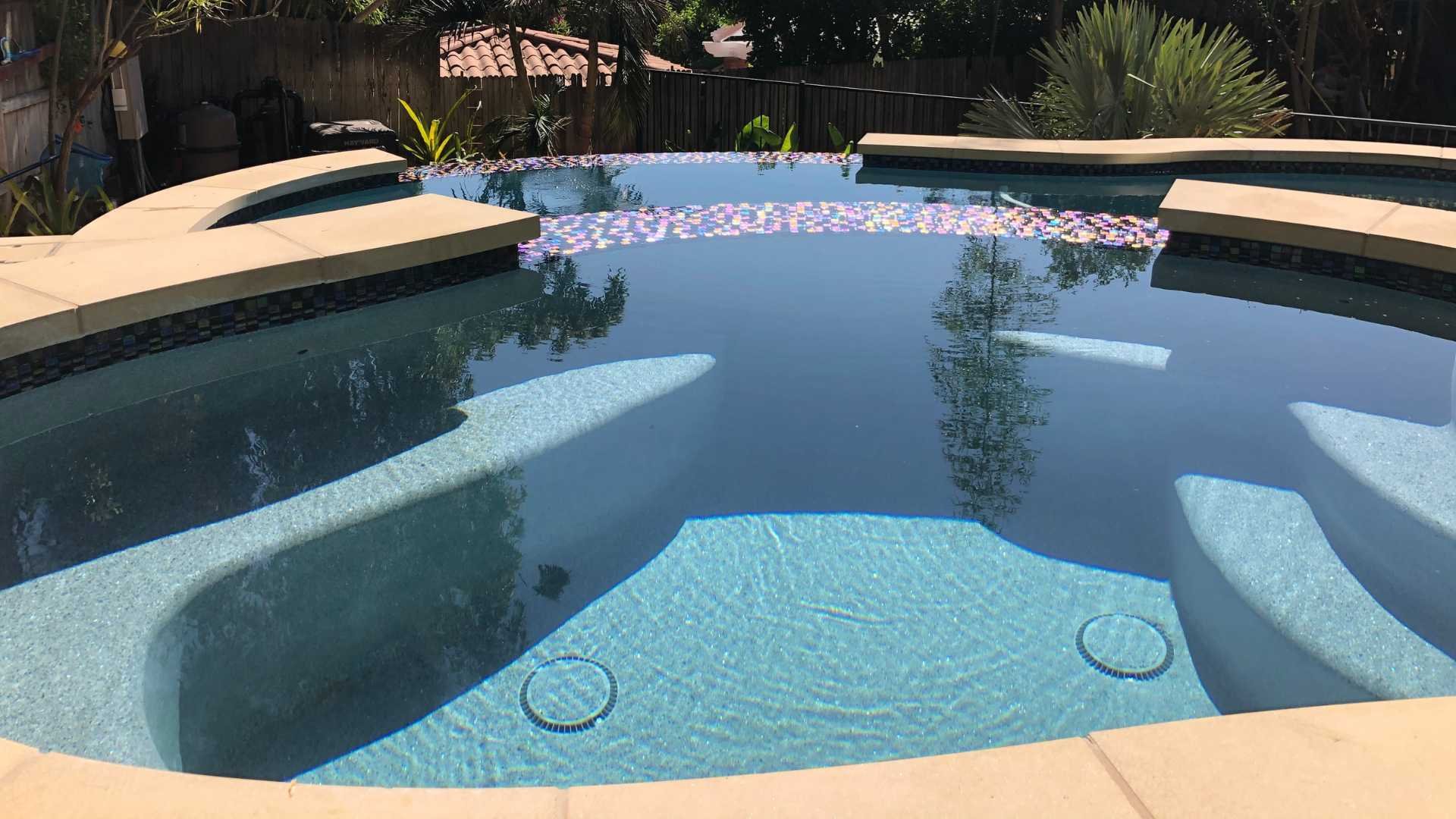 Close-up of the raised spa with glass tiles overlooking the free-form pool with lush greenery in the background.
