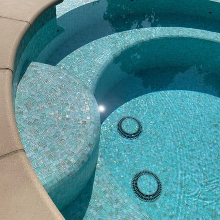 Close-up of the seating area inside a spa, showcasing light blue glass tiles and drain covers