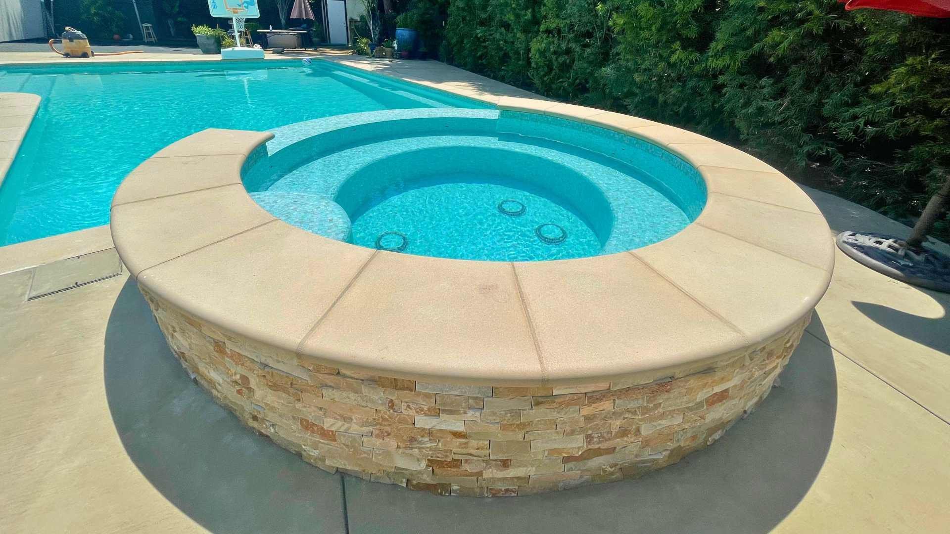 The raised spa with stack stone and a view of the connected pool, which is surrounded by lush greenery.