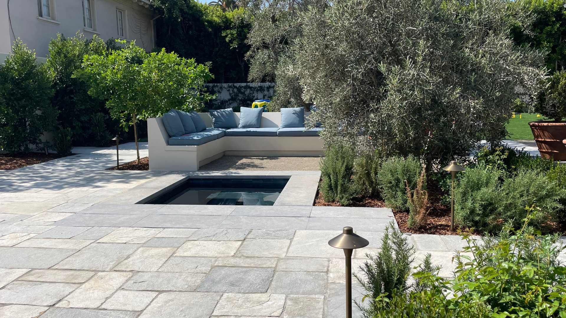 A sunken hot tub surrounded by trees and a landscaped patio with built-in bench seating and potted plants.