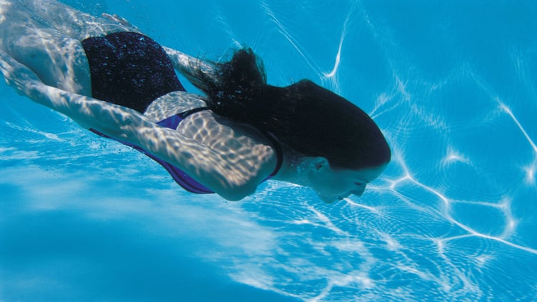 The image displays a woman swimming underwater in a bikini.