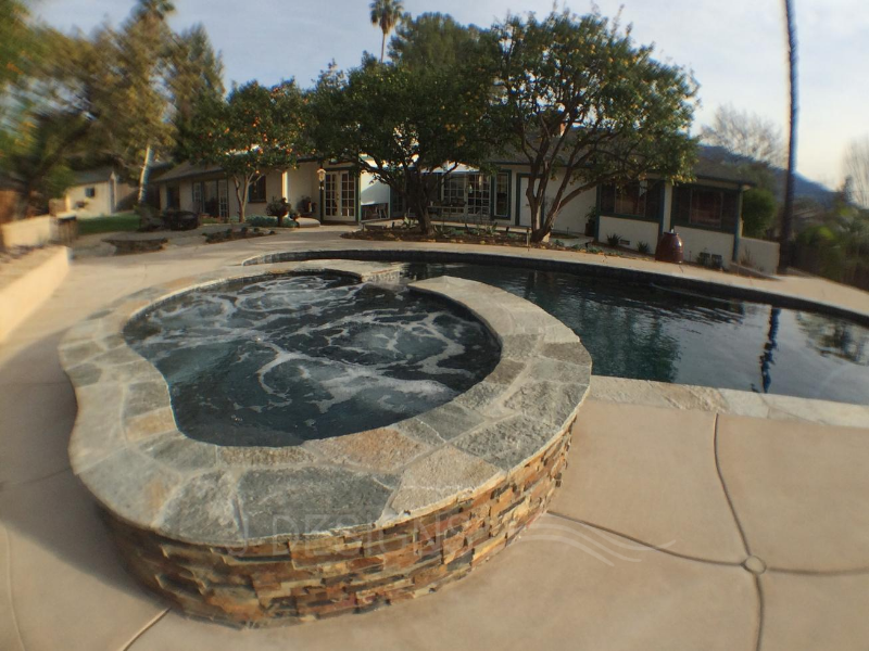 Pool & raised spa, featuring flagstone coping, stacked stone walls & a colorful concrete deck for a remarkable outdoor experience.