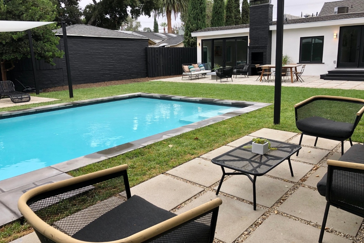 A rectangular pool with a seating area beside it, showcasing outdoor furniture and a green lawn in a minimalist backyard.