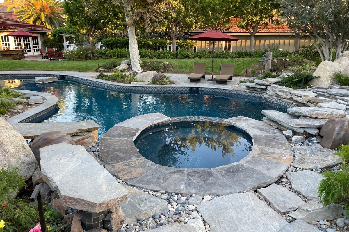 Close-up of a raised spa integrated into a natural stone coping pool with surrounding rock features and glass tile accents.