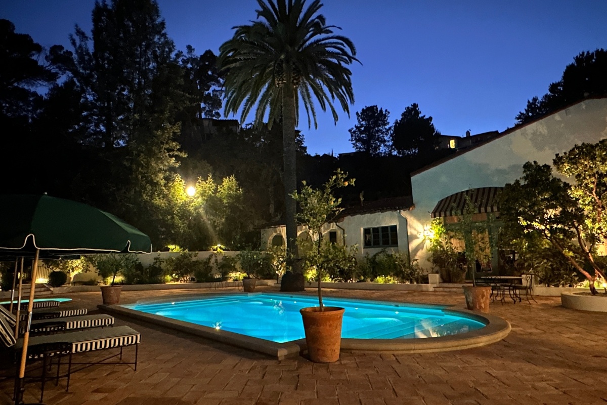 A nighttime view of a fully tiled pool with gold splattered tiles, surrounded by palm trees, Mediterranean-style architecture.