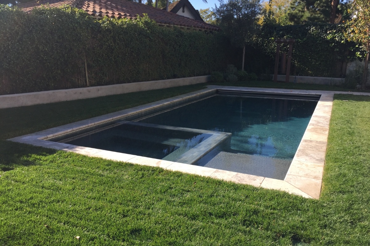 Simple, elegant backyard pool with clean lines, surrounded by a well-manicured lawn and lush privacy hedges.