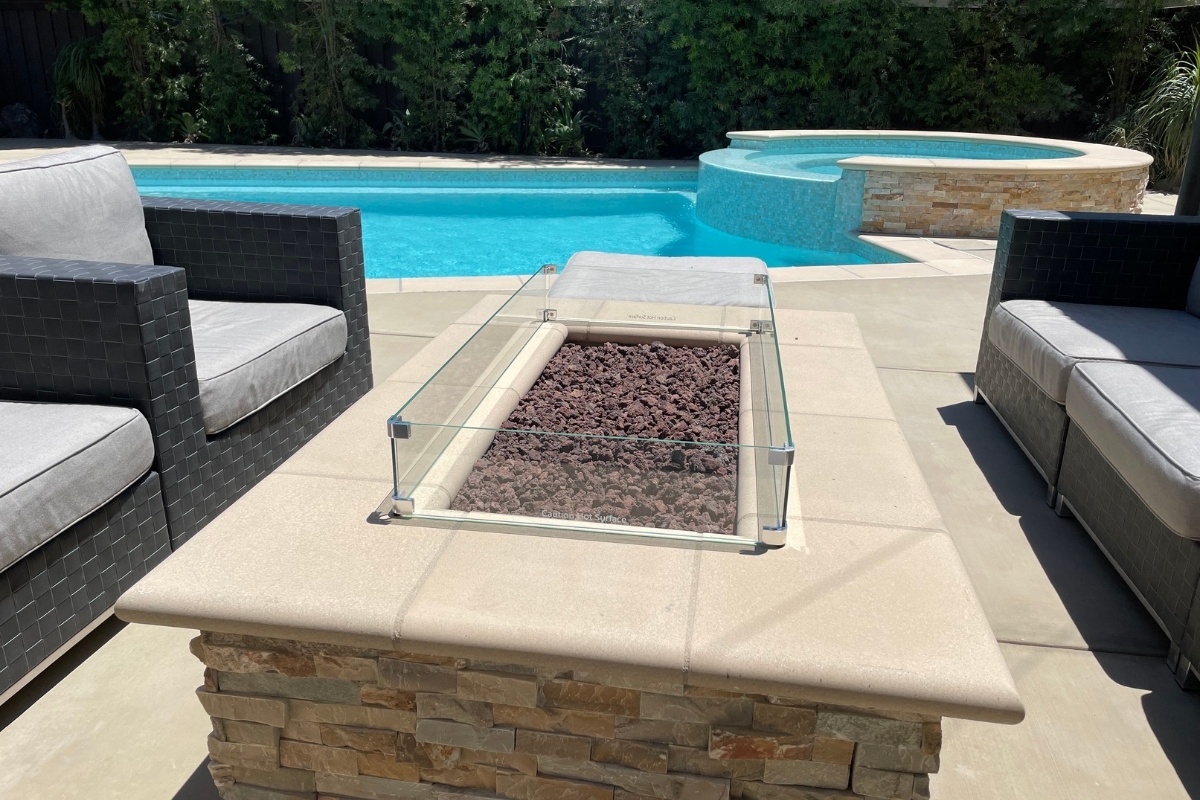 Outdoor fire pit with seating overlooking a pool with a raised spa in a modern backyard.
