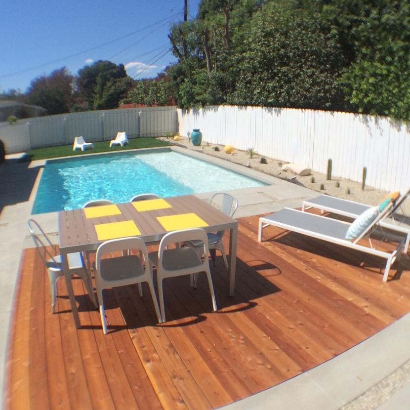 A clear view of a swimming pool featuring a tanning ledge and a wooden deck.