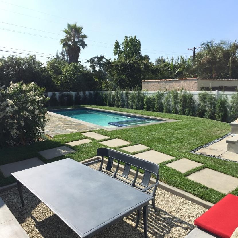 A swimming pool and spa with a rectilinear shape, surrounded by a paver deck and featuring stepping stones.