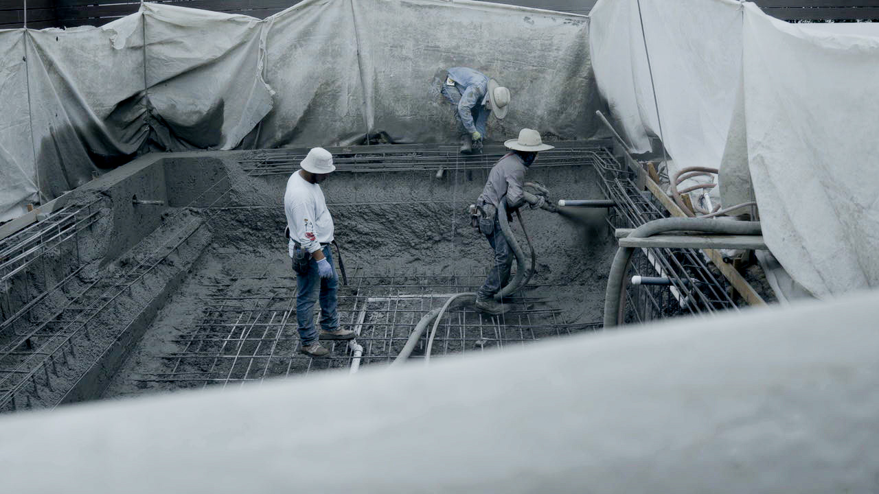 Workers blowing and shaping shotcrete for pool